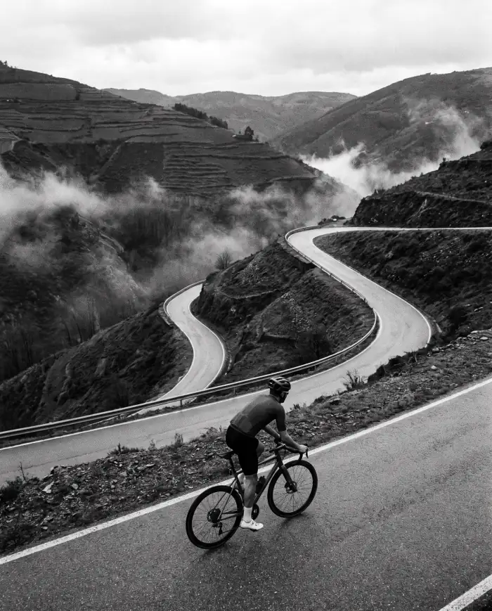 A road cyclist climbing a hairpin road through misty terraced hills
