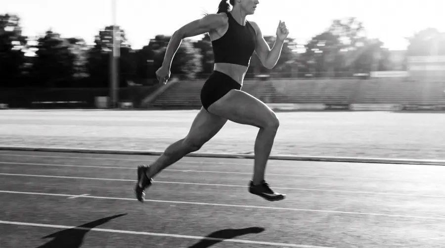 Black-and-white photo of a sprinter mid-stride on an outdoor track in low sun